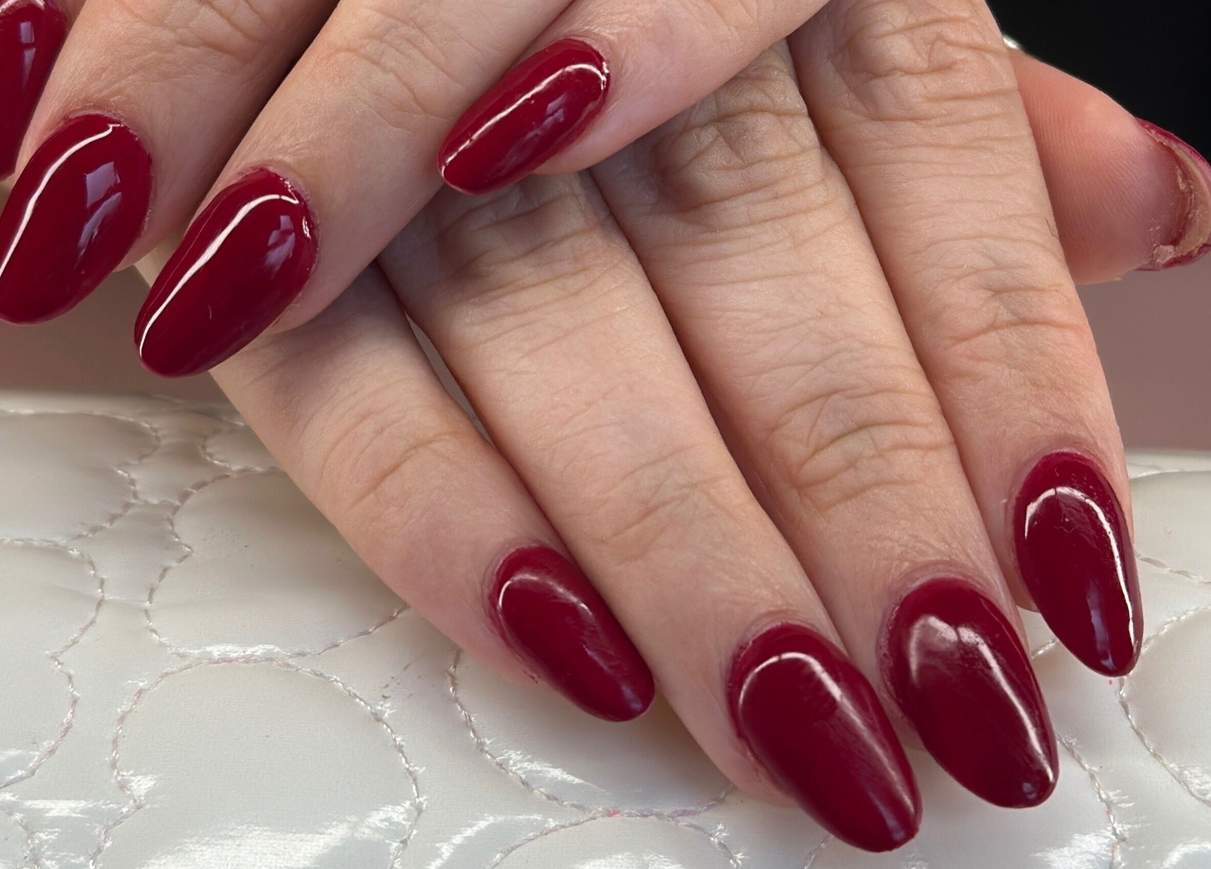 Elegant red nails at Glow Nails, Dublin, County Dublin, IE. Perfectly manicured hands on white cushion.