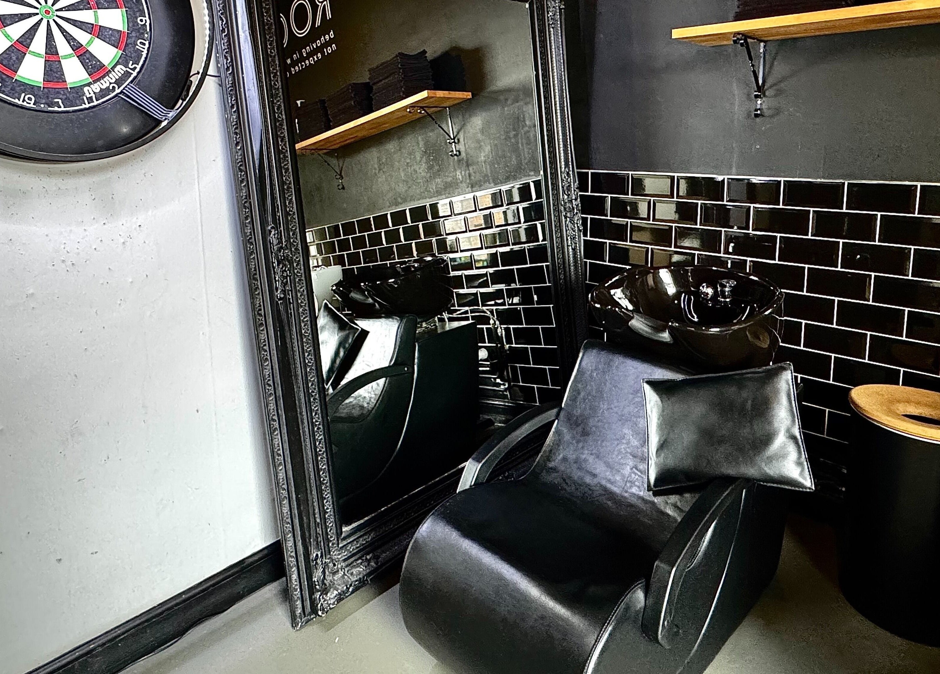 Modern salon chair and sink in Simply Rogue, Darlington, England, GB with sleek black tiles and mirror.