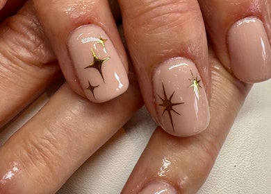 Elegant celestial nail art at Aster Beauty, Fakenham, England, GB, featuring gold star designs on nude polish.