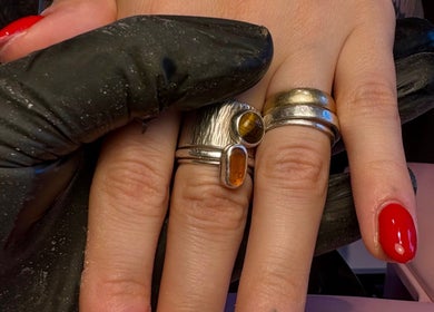 Close-up of a manicured hand with red nails and silver rings at Aster Beauty, Fakenham, England, GB.