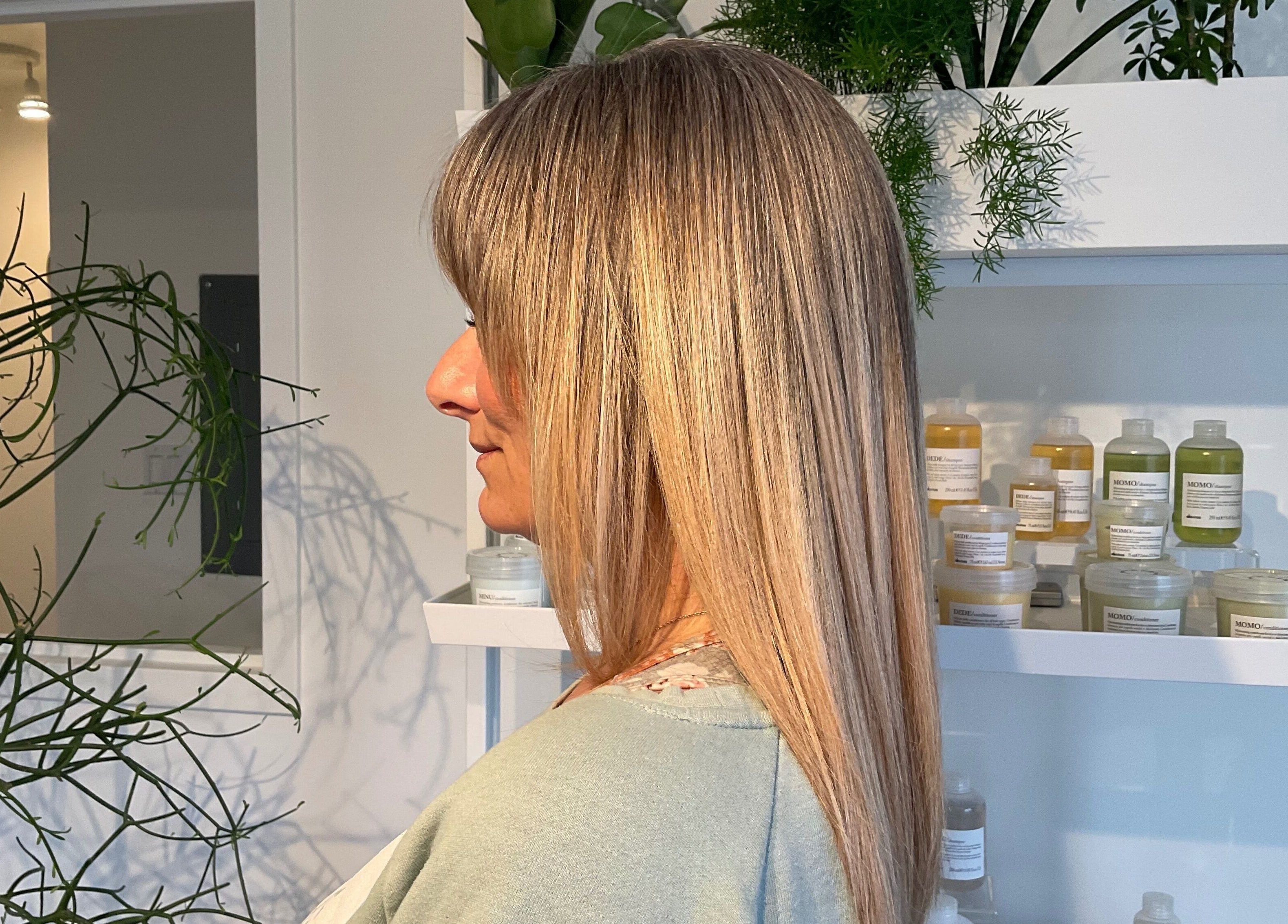 Femme aux cheveux lisses chez Village Coiffure à Saint-basile-le-grand, Québec, CA. Produits capillaires en arrière-plan.
