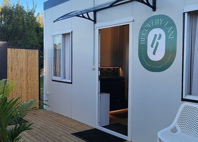 Entrance of Recovery Lane, a therapy studio in Waiuku, Auckland, NZ, with wooden deck and greenery.