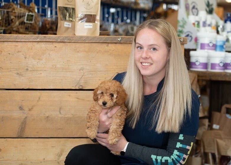 A woman holding a small puppy at Susie Qs Dog Grooming in Copplestone, England, GB, surrounded by pet supplies.