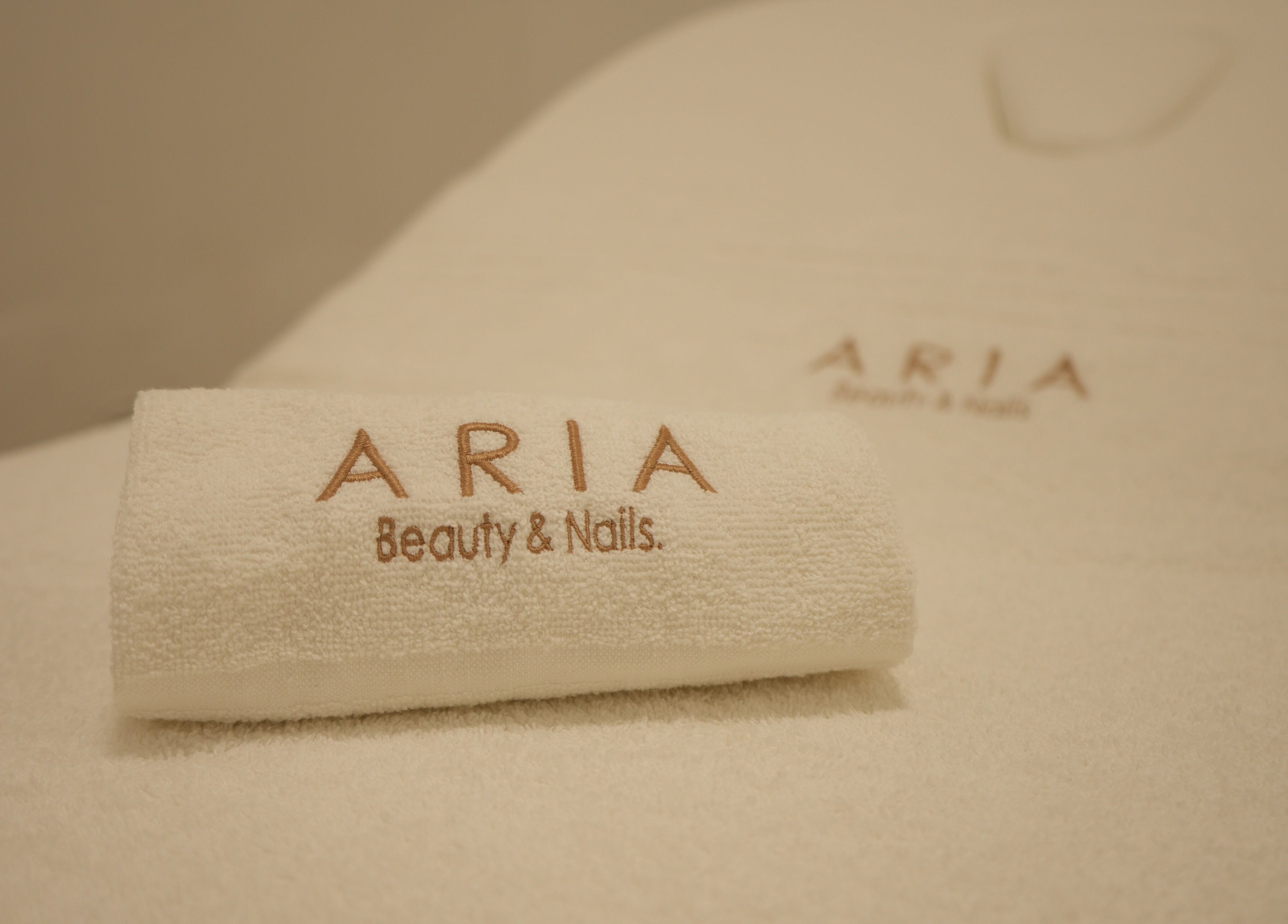 Asciugamano bianco con logo Aria Beauty & Nails a Grottaglie, Puglia, IT per un'esperienza di lusso.