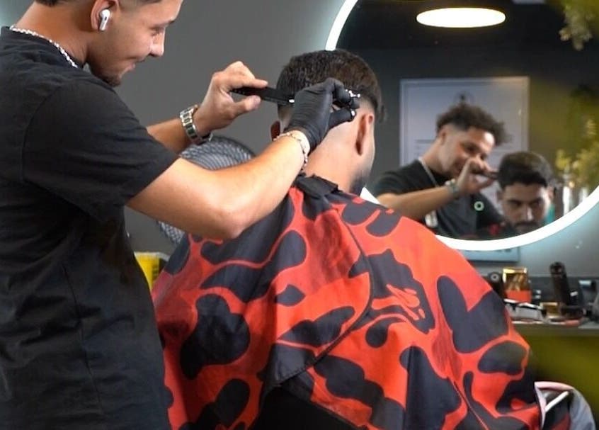 Stylist at The Barber, London, England, GB expertly trims a client's hair in a stylish, modern setting.