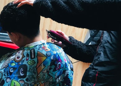 Corte de cabello en M10 Barberia, Padre Las Casas, Araucanía, CL con una máquina de cortar y capa colorida.