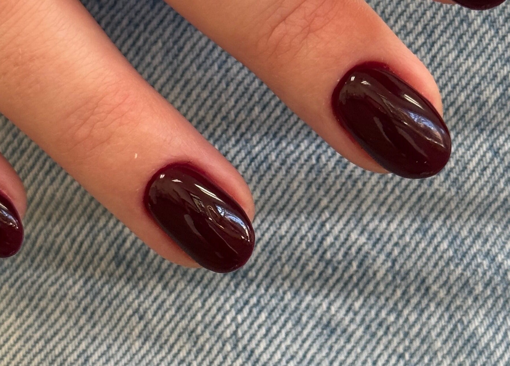 Elegant dark red manicure at Dangina Studio, Aurora, Illinois, US on a blue fabric background.
