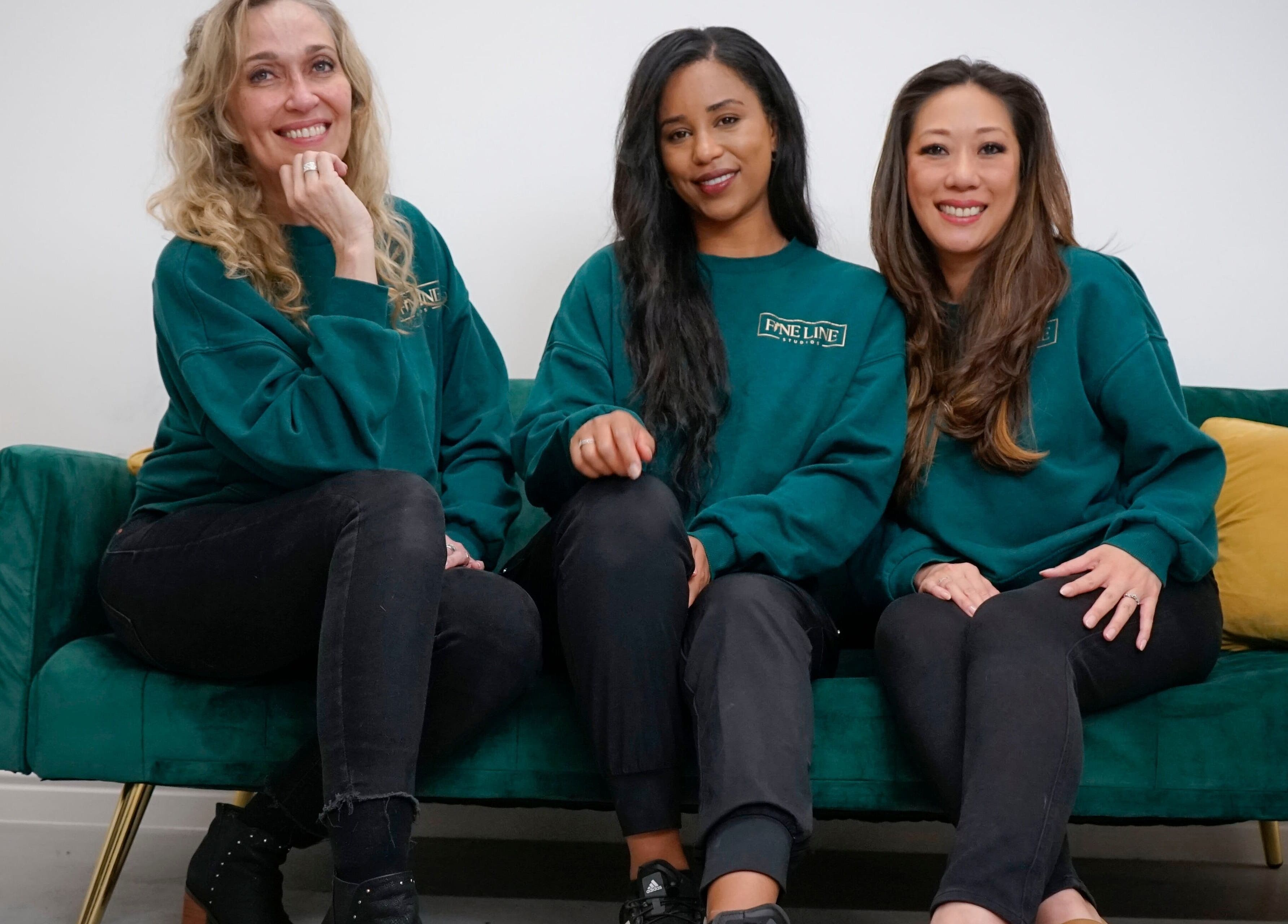 Friendly team at Fine Line Studios, London, England, GB, sitting on a green couch wearing matching green sweaters.