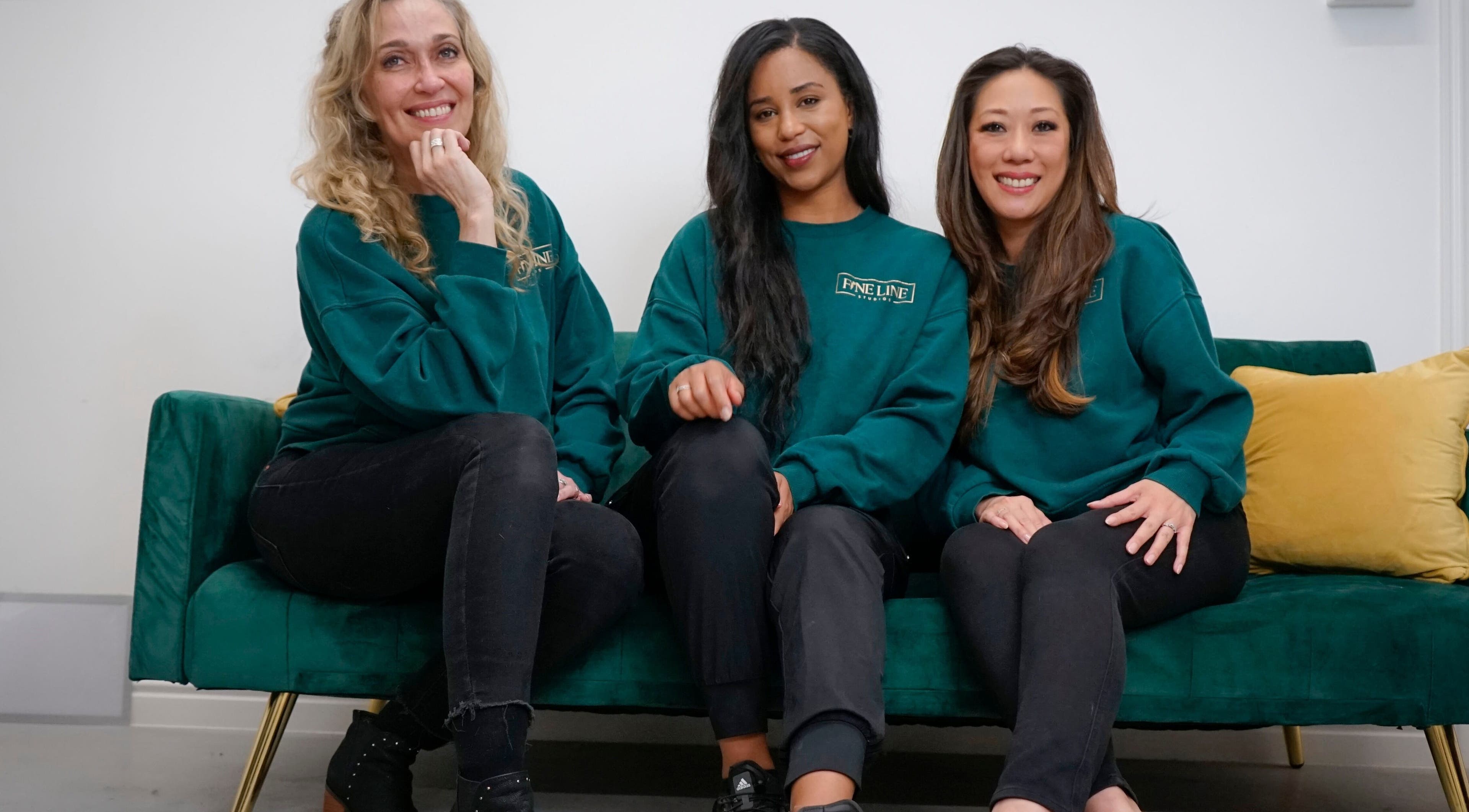 Friendly team at Fine Line Studios, London, England, GB, sitting on a green couch wearing matching green sweaters.