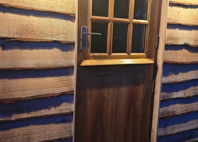 Wooden door entrance of Flutters Lash Studio in Washingborough, England, GB, warmly lit by soft lighting.