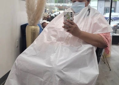 Client at Silky | The Healthy Hair Experts in New York, covered in cape, holding phone, enjoying hair service.