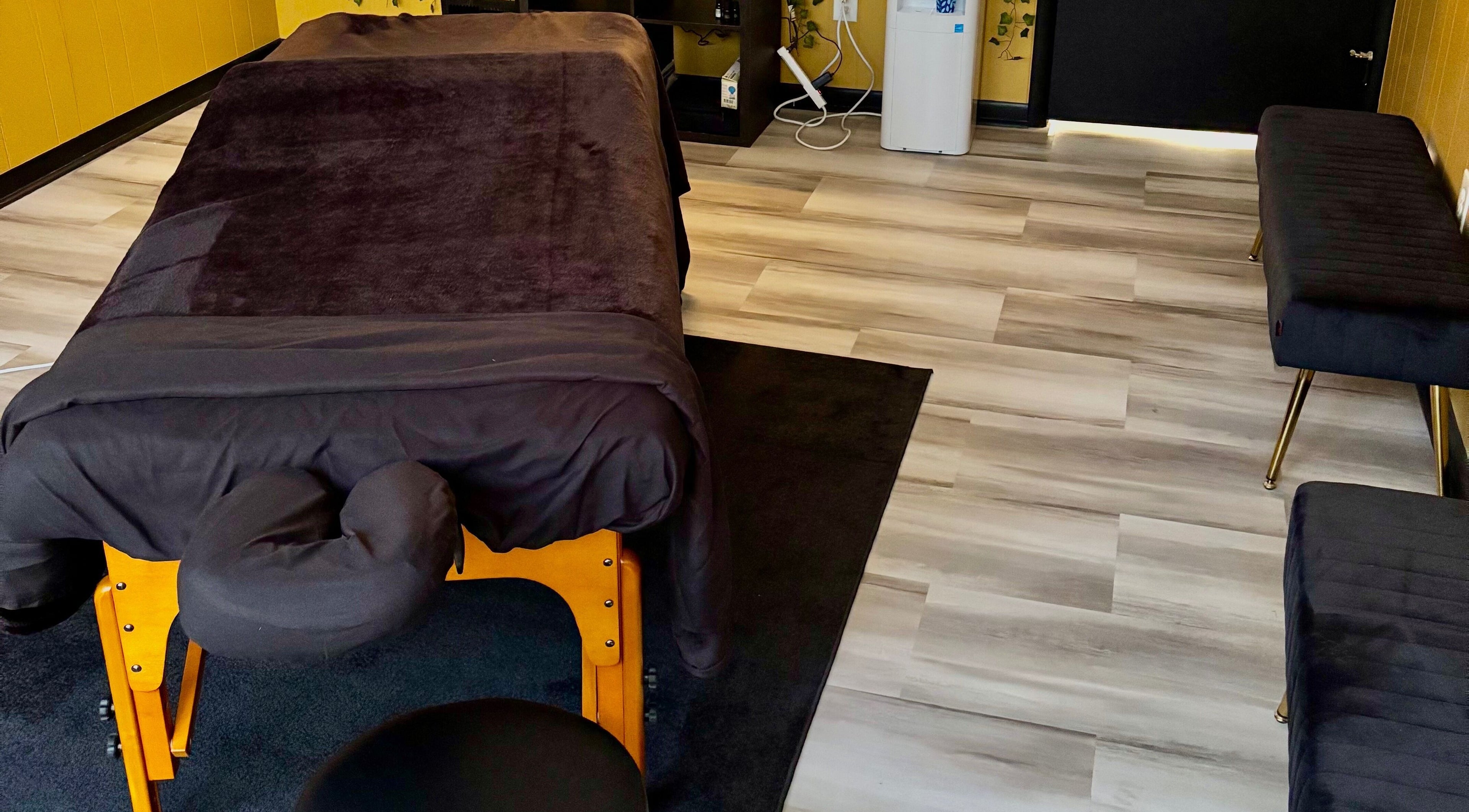 Cozy massage room setup at Serenity’s Remedies in Toledo, Ohio, US featuring a massage table and plush seating.