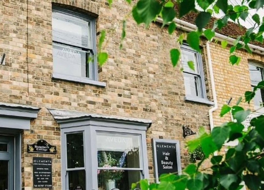Exterior of Pure Elements salon in Long Melford, England, with rustic brick and lush greenery.