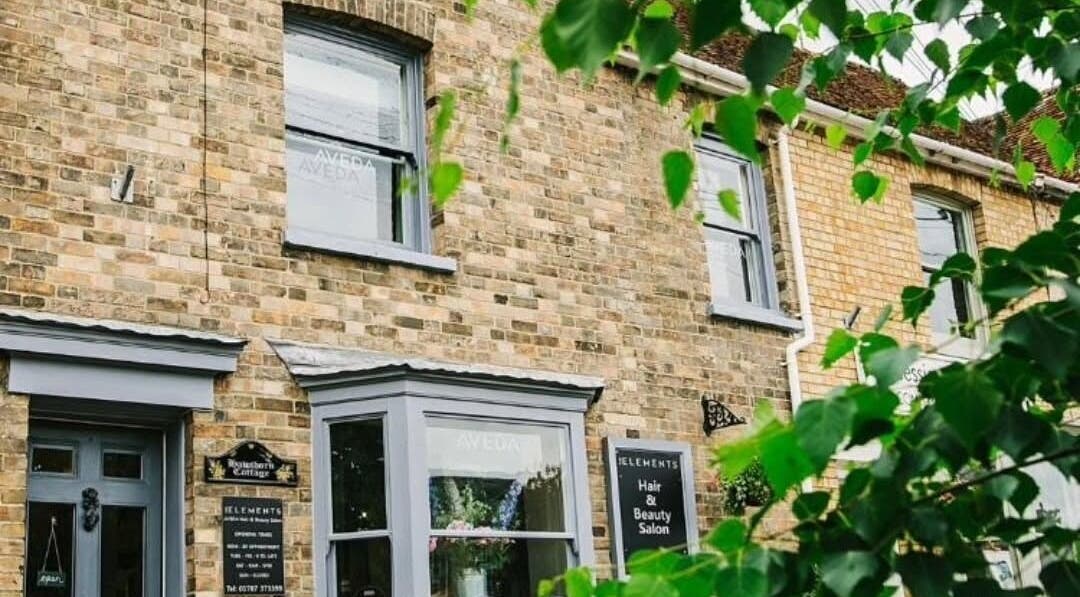 Exterior of Pure Elements salon in Long Melford, England, with rustic brick and lush greenery.