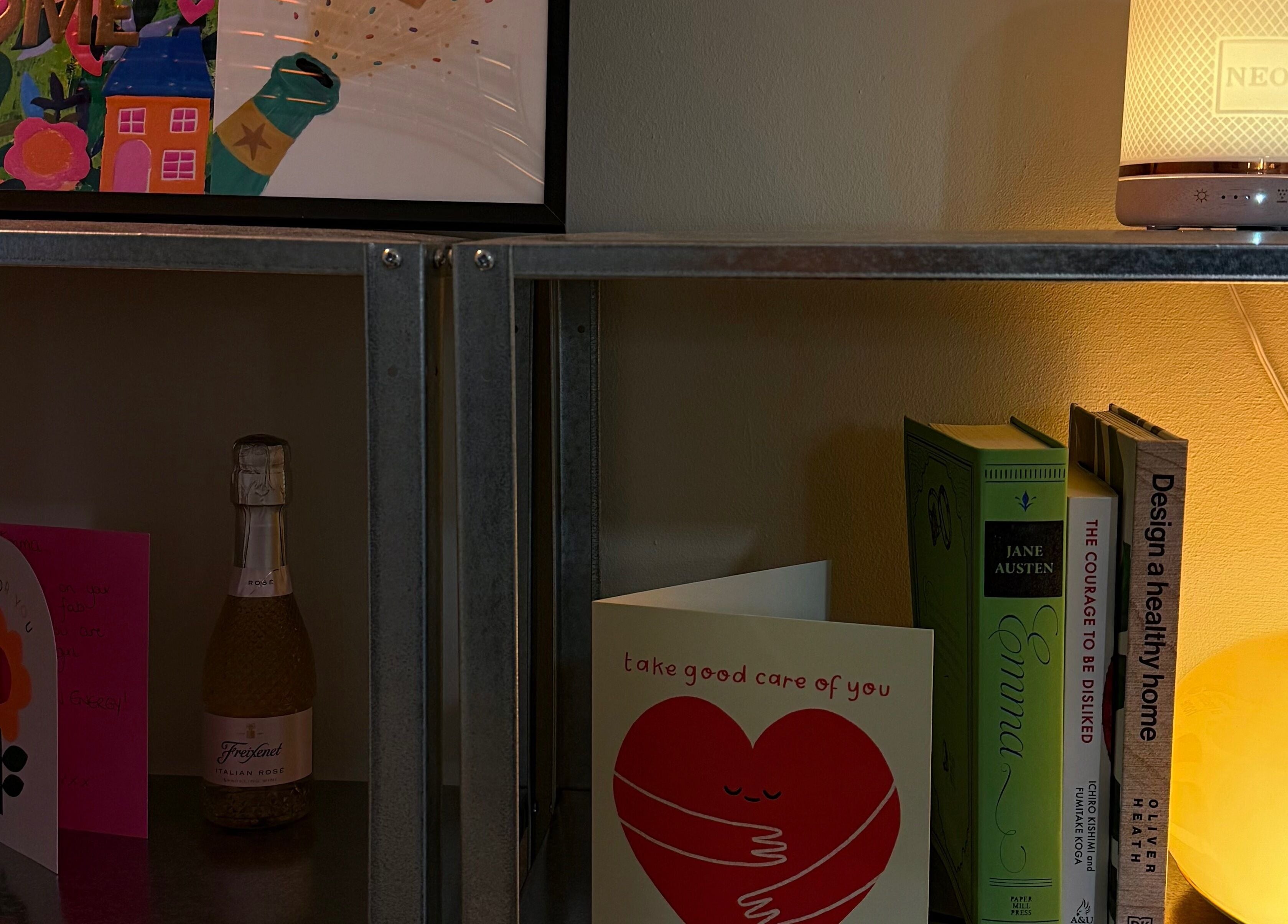 Warm-lit shelf at emstudio, Clydebank, Scotland, GB, with books, cards, and a glowing lamp.