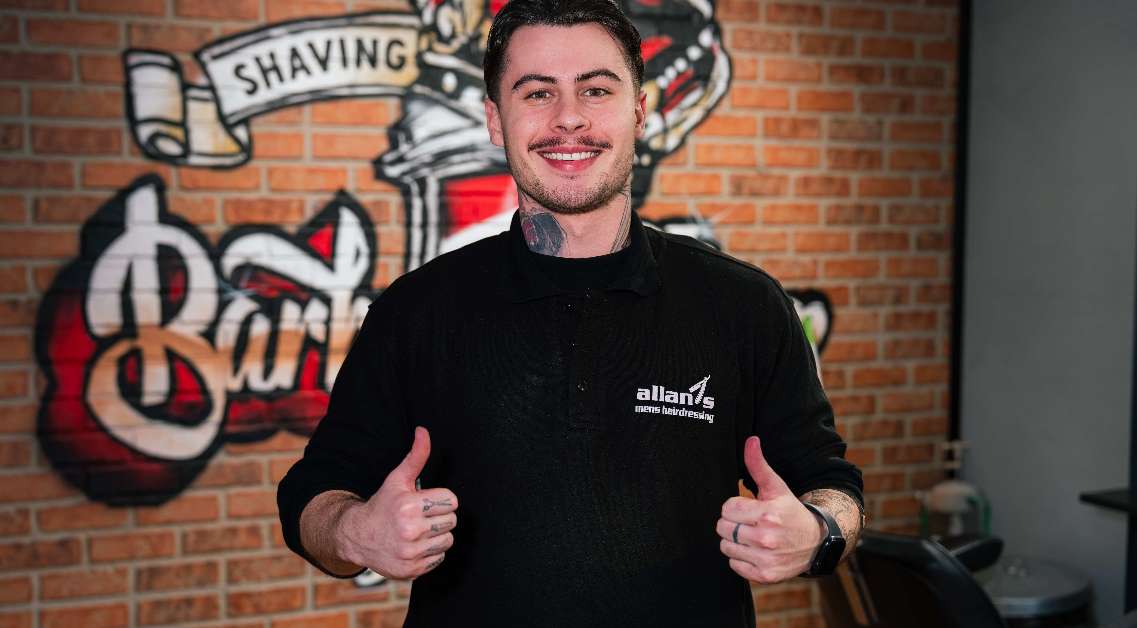Barber at Allan's Men's Hairdressing - Warrabrook, New South Wales, AU, smiles confidently in front of salon decor.