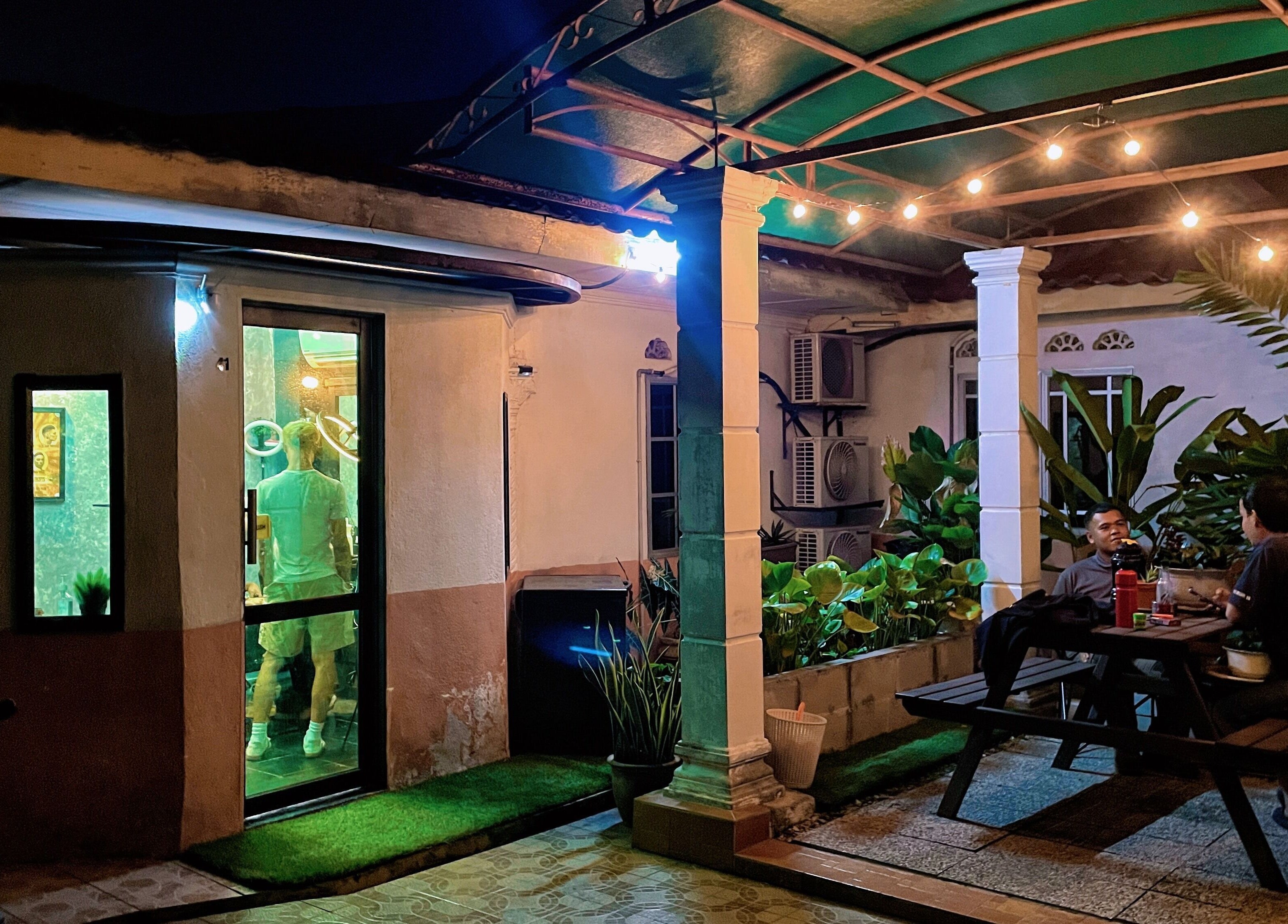 Night view of Room41 Barber's inviting patio in Klang, Selangor, MY, with lush plants and warm ambiance.