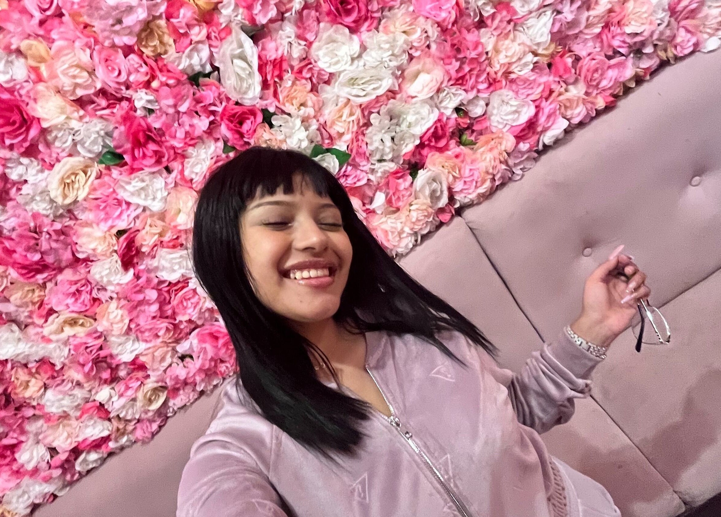 Mujer sonriente en mural floral rosa en Salon rosa Ayleenda uñas pestañas cursos joyas de Quilpué, Valparaíso, CL.