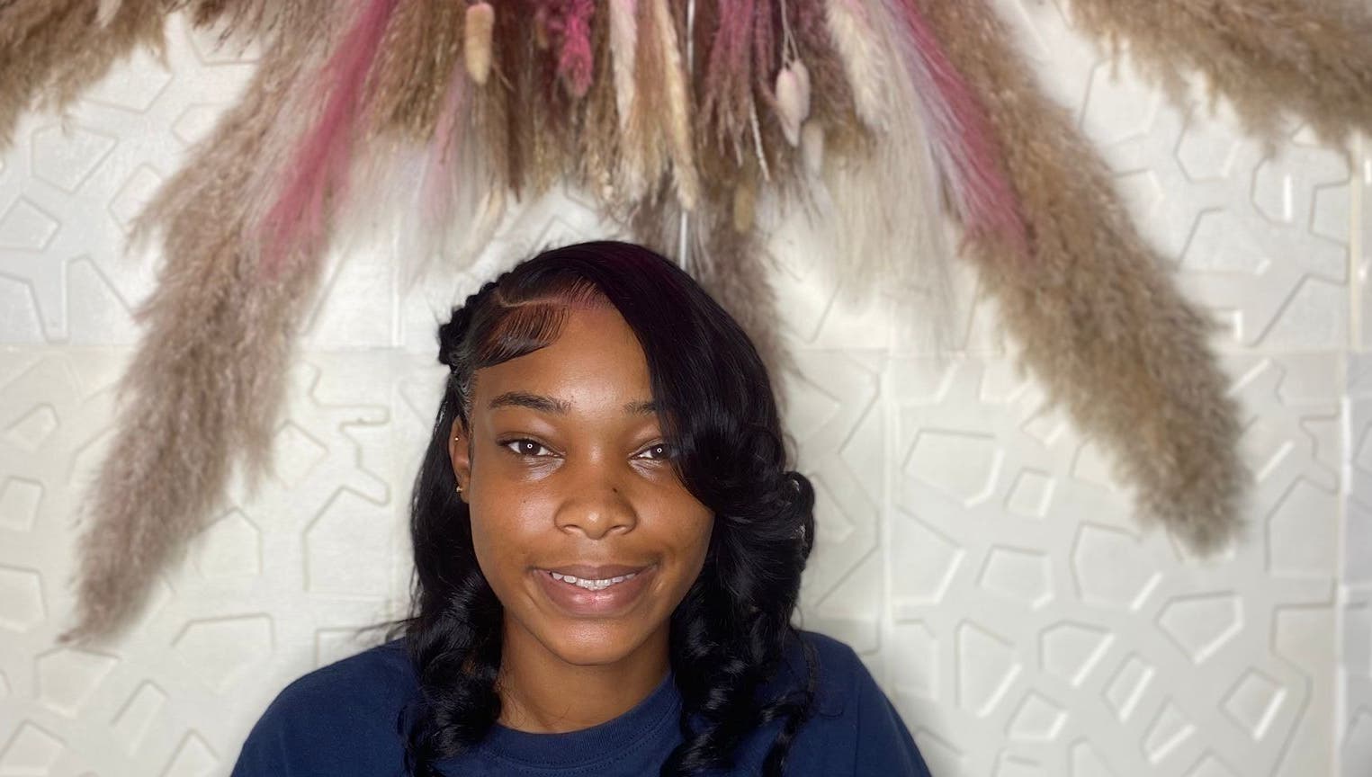 Smiling woman with styled hair at Styles By Kera, Roseau, Saint George Parish, DM, under decorative display.