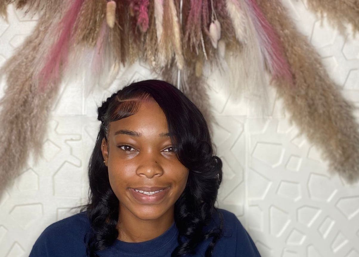 Smiling woman with styled hair at Styles By Kera, Roseau, Saint George Parish, DM, under decorative display.