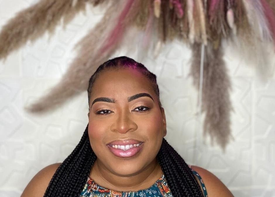 Smiling woman at Styles By Kera, Roseau, Saint George Parish DM, with braided hair and decorative background.