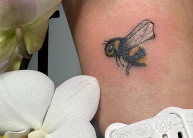 Bee tattoo surrounded by orchids at Hellhouse salon, Norwich, England, GB.
