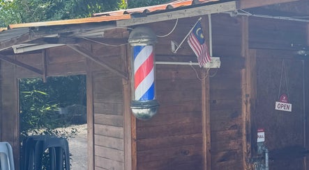 Barber pole at Aididthebarber, a rustic wooden venue in Klang, Selangor, MY, with a Malaysian flag and open sign.