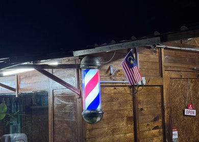Aididthebarber's rustic exterior with a glowing barber pole in Klang, Selangor, MY.