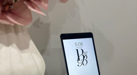 Tablet displaying BROWS BABE logo at Melbourne, Victoria, AU with nearby pink flowers.