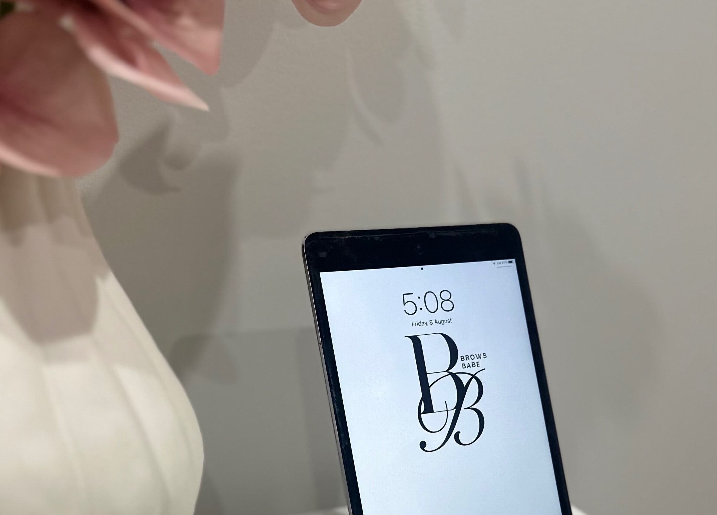 Tablet displaying BROWS BABE logo at Melbourne, Victoria, AU venue with soft pink flowers.