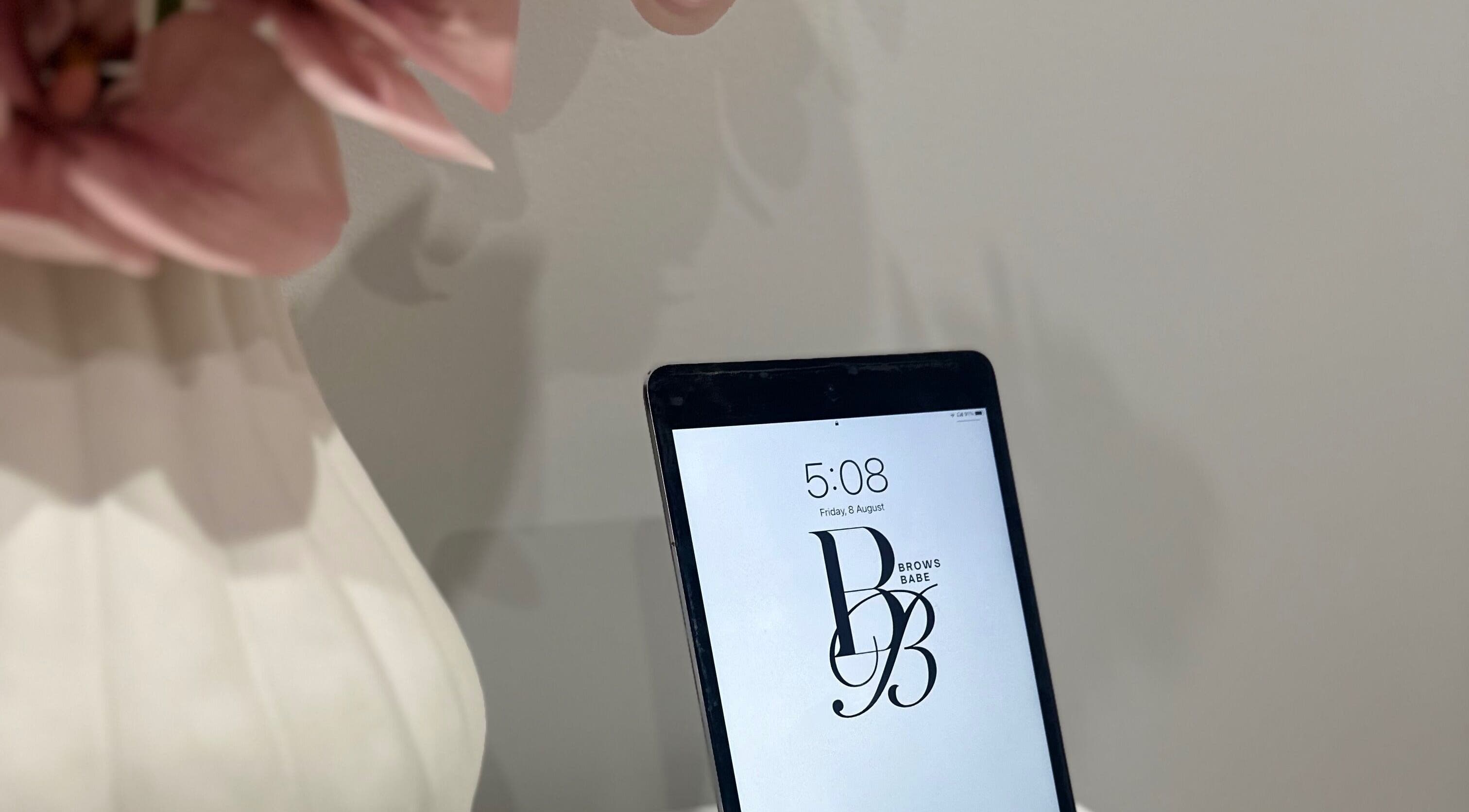 Tablet displaying BROWS BABE logo at Melbourne, Victoria, AU venue with soft pink flowers.