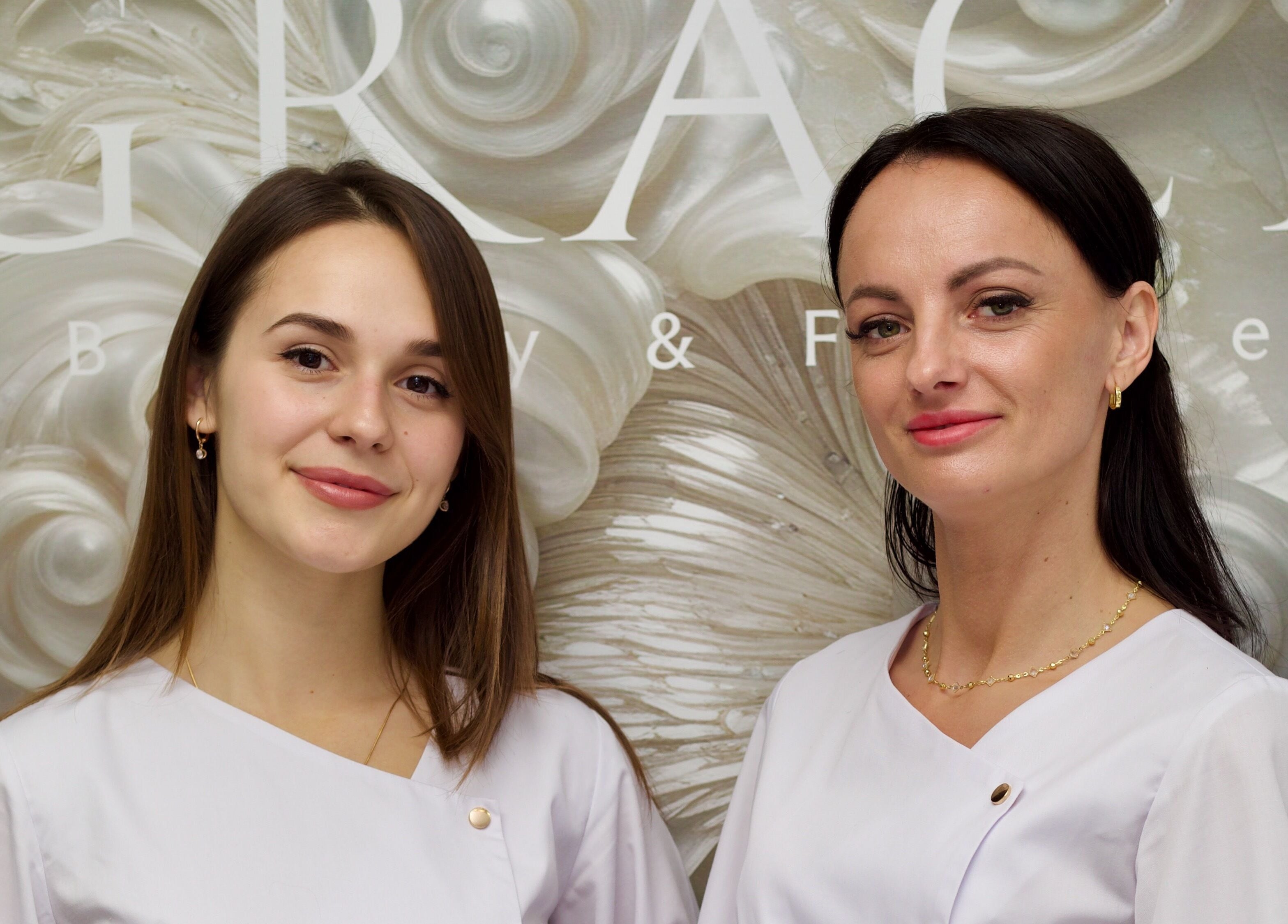 Two smiling professionals at GRACE body&face, Glyfada, GR, in front of an elegant backdrop.