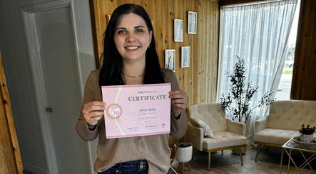 Smiling woman holding certificate at Aesthetics by Juhliah J M, Bend, Oregon, US. Modern wood-paneled interior.