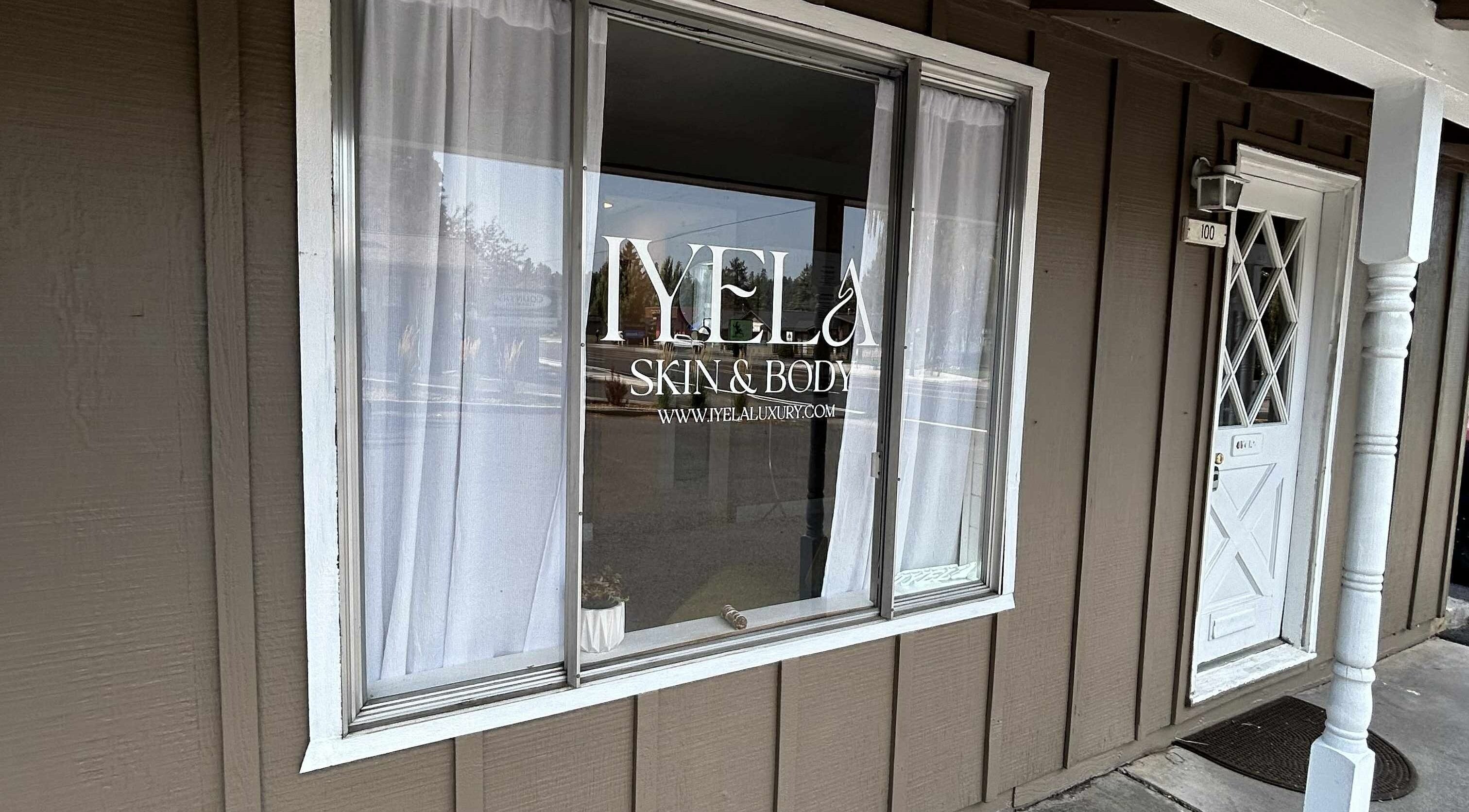 Shopfront window of Aesthetics by Juhliah J M in Bend, Oregon, US, reflecting a serene street view.