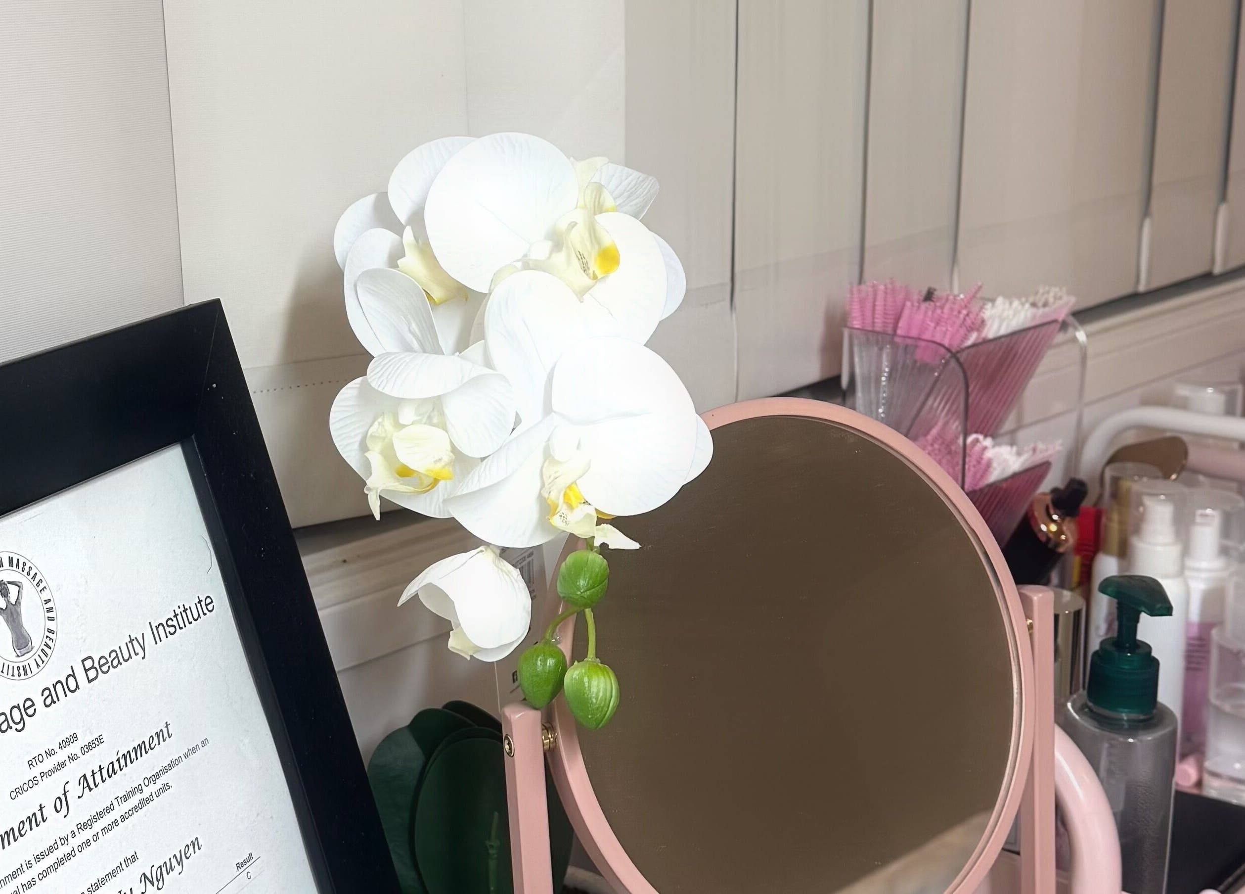 A serene beauty setup at V's Lashes, Hamlyn Terrace, New South Wales with orchid, mirror, and beauty products.