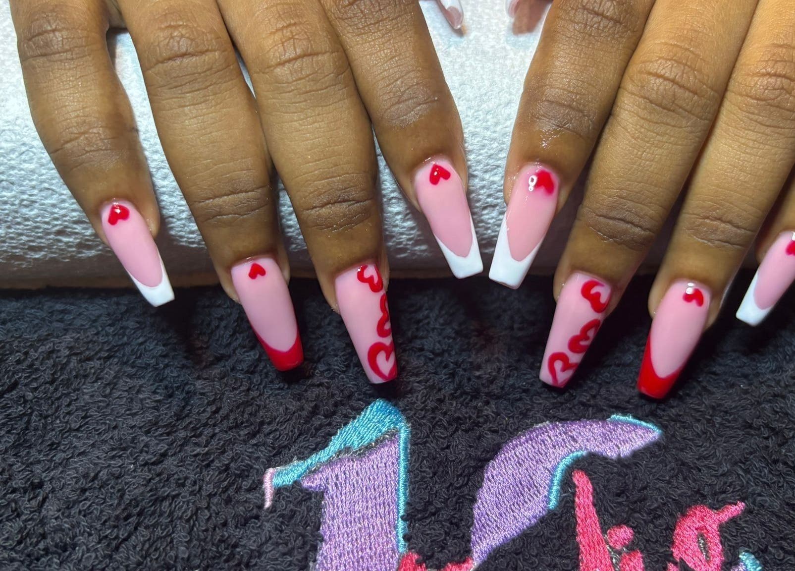 Stylish heart-themed nail art at STUDIO 10, FREEPORT, Grand Bahama, BS. Pink and red design on hands.