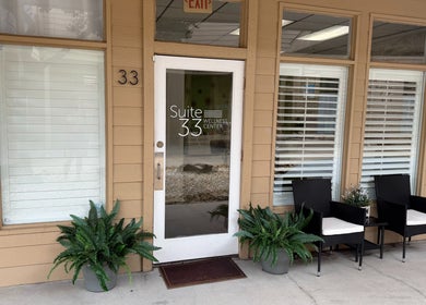 Entrance of Bare Essence Spa in Gulf Breeze, Florida, US, featuring stylish chairs and green plants.
