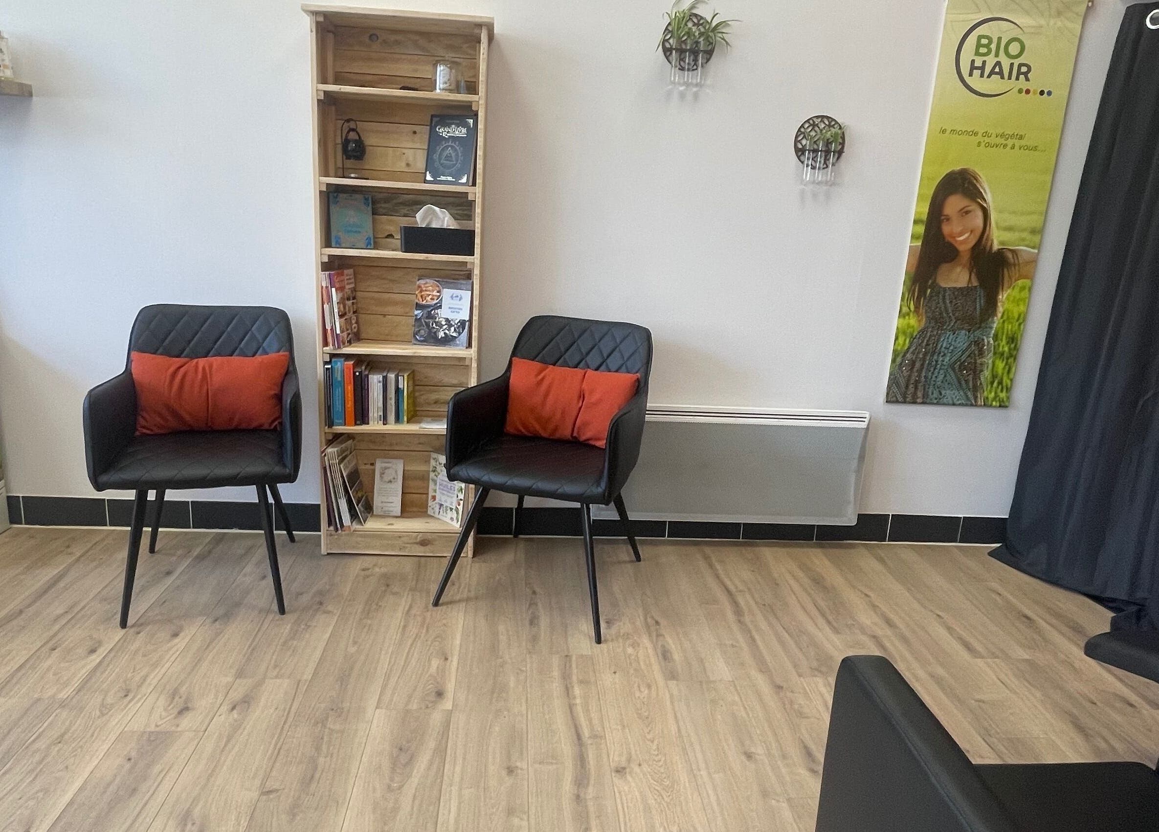 Coin salon élégant chez Coiffure By Cha à Uzer, Auvergne-rhône-alpes, FR avec fauteuils et étagère en bois.