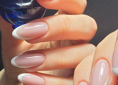 French manicure at Nataliia Demi Nails, London, England, GB. Close-up of elegant nails holding a blue bottle.