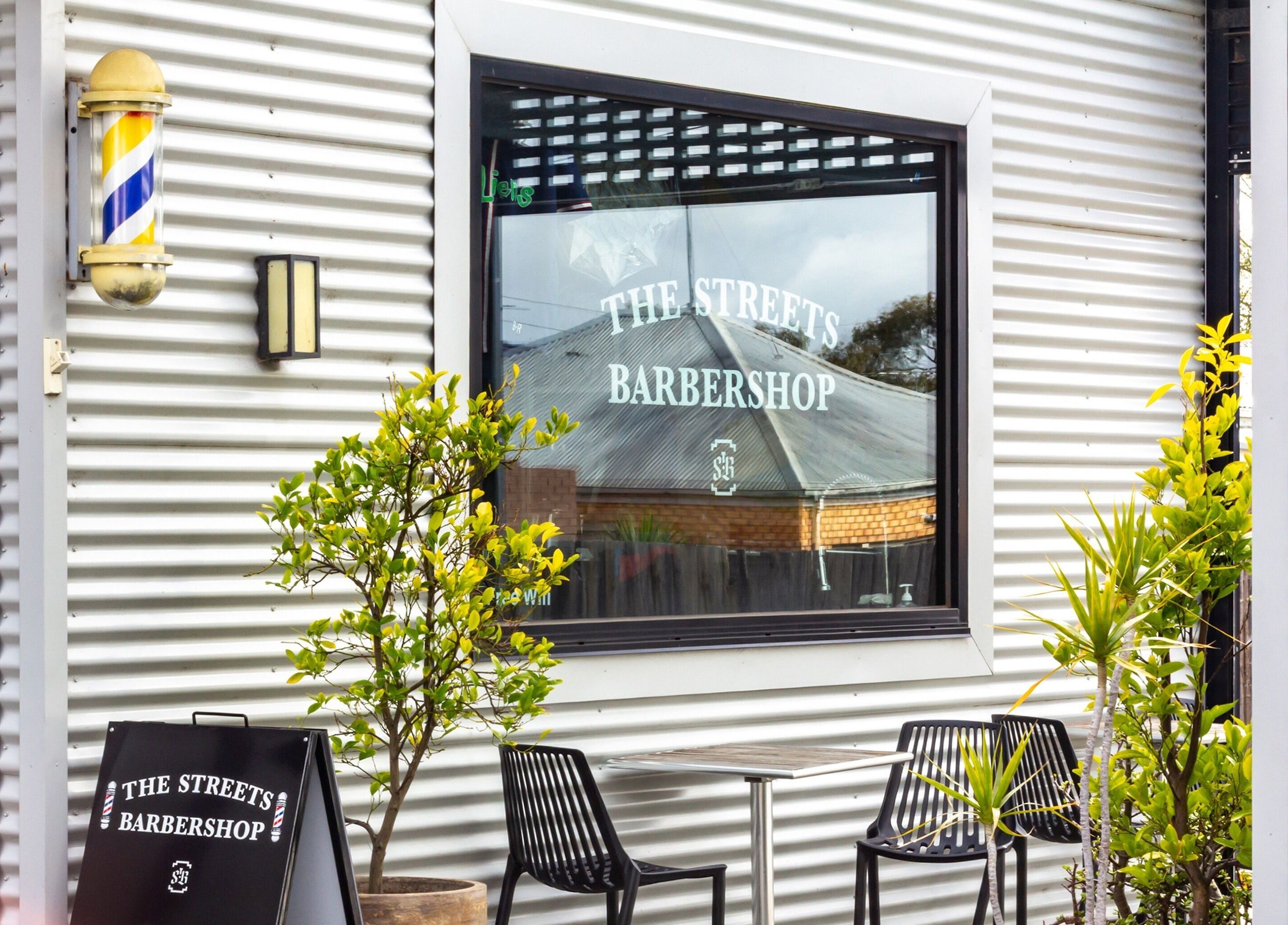 Exterior of The Streets Barbershop in Geelong West, Victoria, AU, showing stylish black chairs and plants.