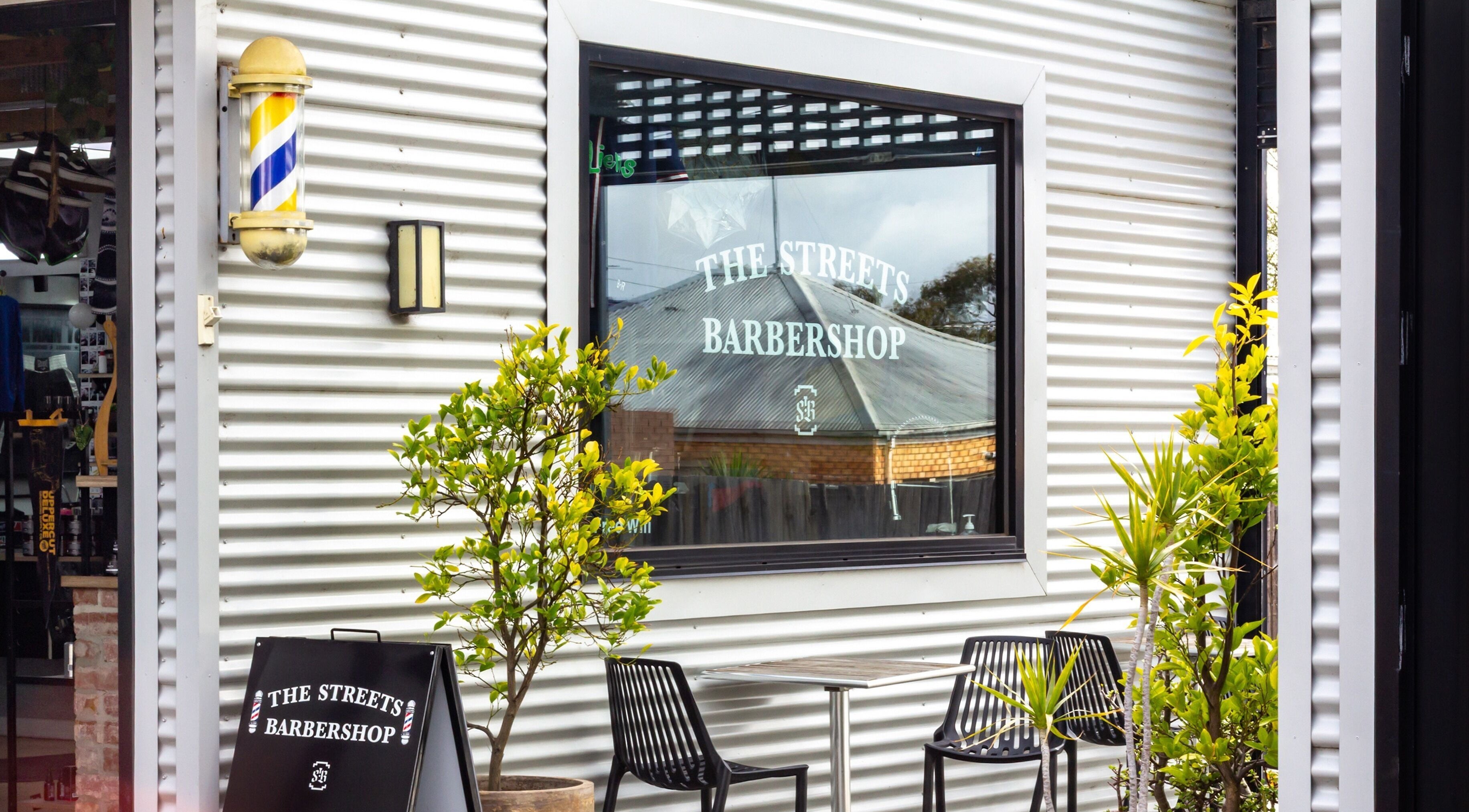 Exterior of The Streets Barbershop in Geelong West, Victoria, AU, showing stylish black chairs and plants.
