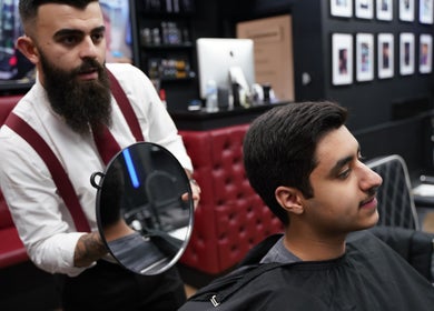 Barber styling customer's hair at Wicked Barber in London, England, GB. Cozy red leather chairs fill the shop.