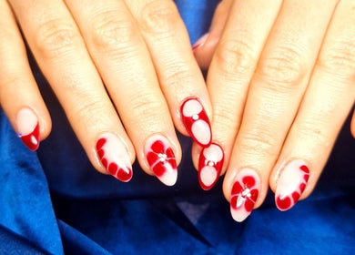 Intricate red nail art at Poise & Polish Beauty Bar, Cape Town, Western Cape, ZA on elegant hands over blue fabric.