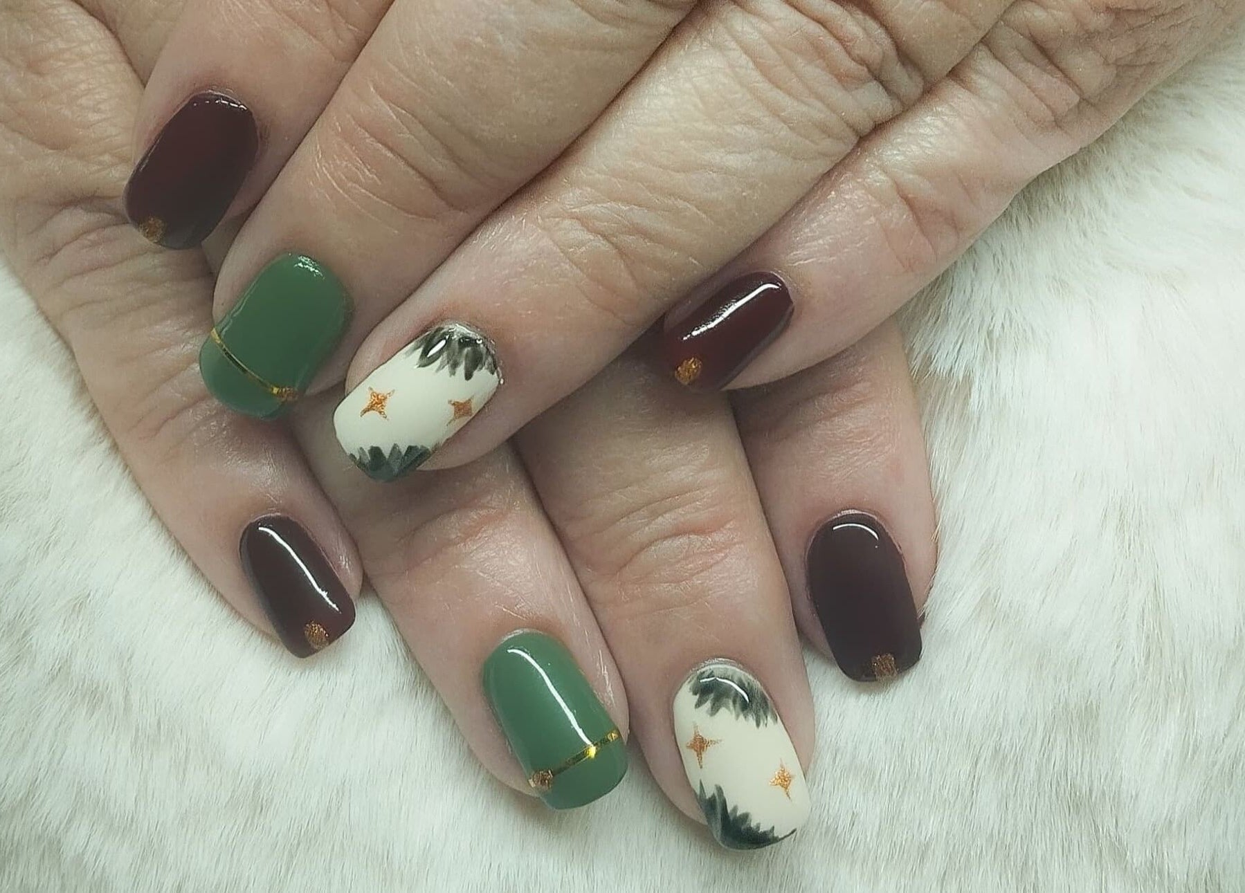 Elegant nail art at Nails By Kim, Pretoria, Gauteng, ZA showcases green and maroon designs on white fur.