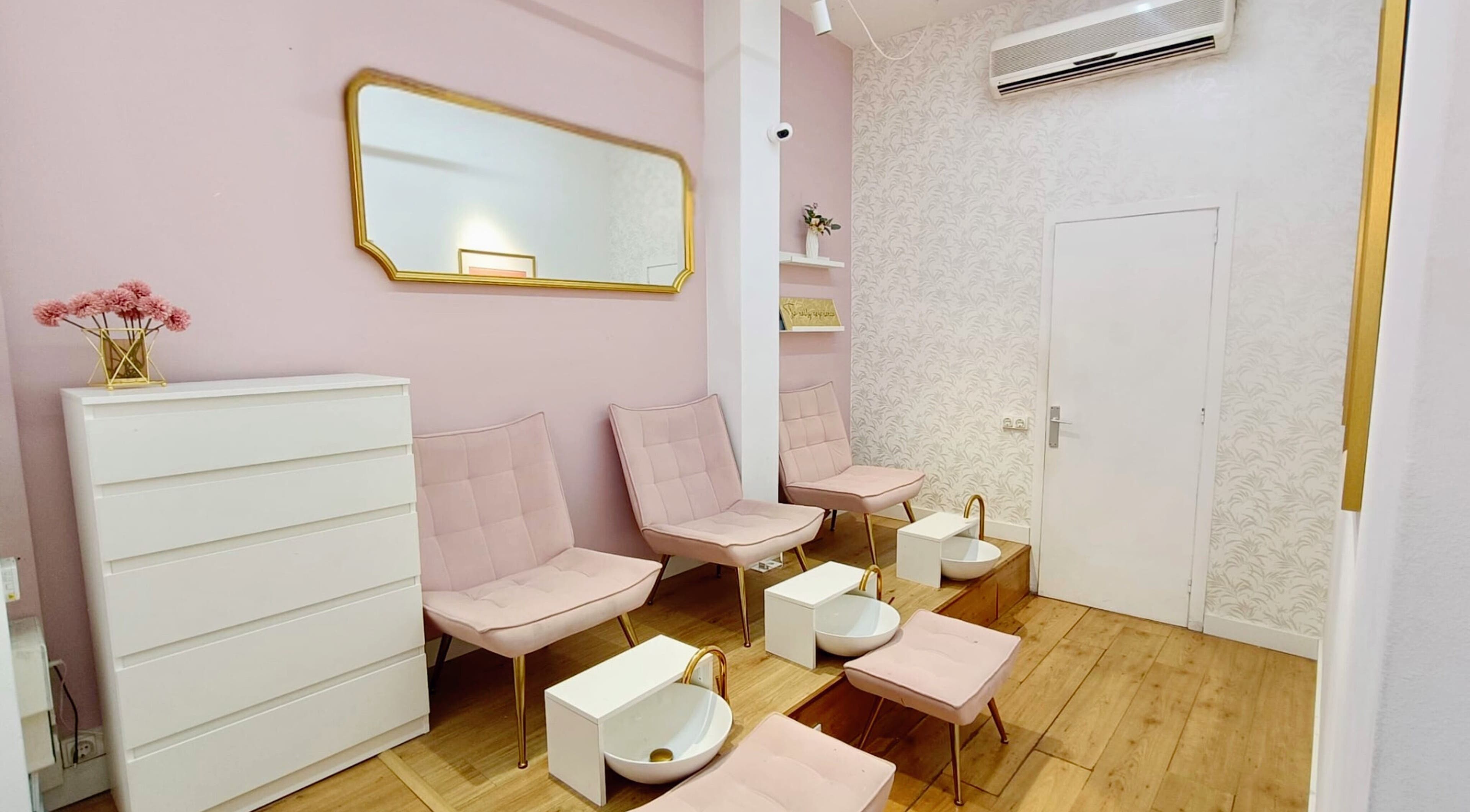 Moderno interior de GLAM Nails Studio - Guillem Tell, en Barcelona, con elegantes sillas rosadas y decoración floral.