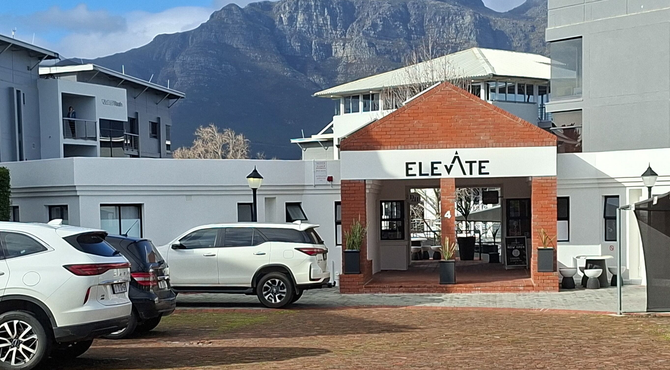 Entrance of Elevate building near Hair by Dawid, Stellenbosch, Western Cape, ZA, with mountains in background.