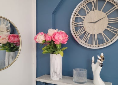 Décor élégant chez Magnifi'sens, Coubron, Île-de-France, avec horloge et fleurs roses en vase marbré.