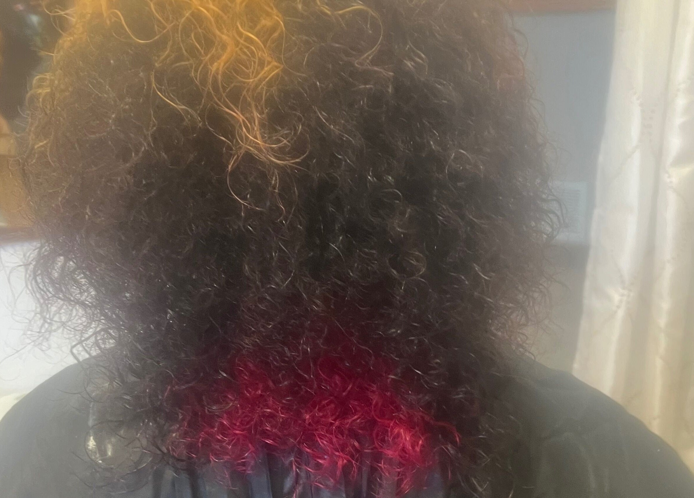 Vibrant curly hairstyle with red tips at Tasja’s Style Studio, Madison, Wisconsin, US.