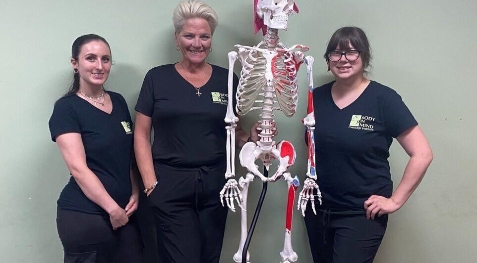 Instructors at Body in Mind Massage Institute - Toms River, NJ, pose with a skeleton model.