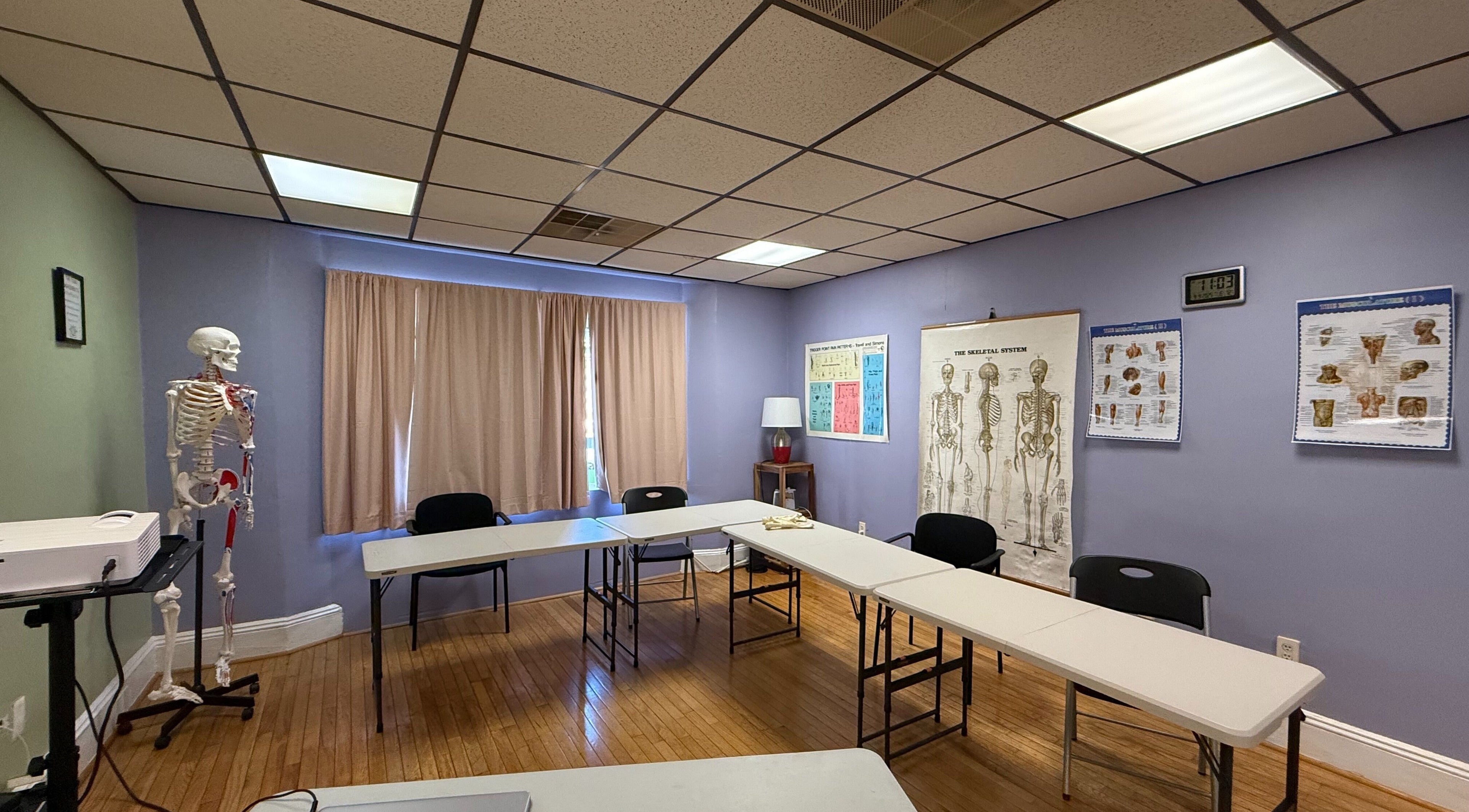 Classroom at Body in Mind Massage Institute - West New York, NJ showing chairs and anatomical posters.